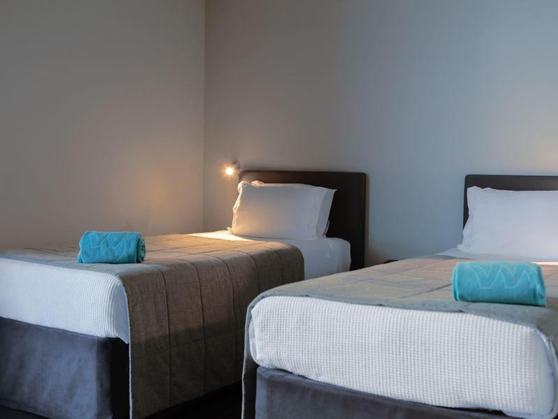 Due letti singoli con lenzuola bianche e asciugamani blu in una stanza d'hotel semplice.