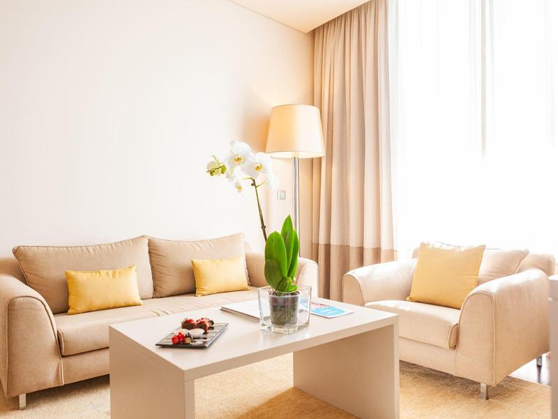 Soggiorno luminoso con sedute beige, cuscini gialli e tavolino bianco con pianta.