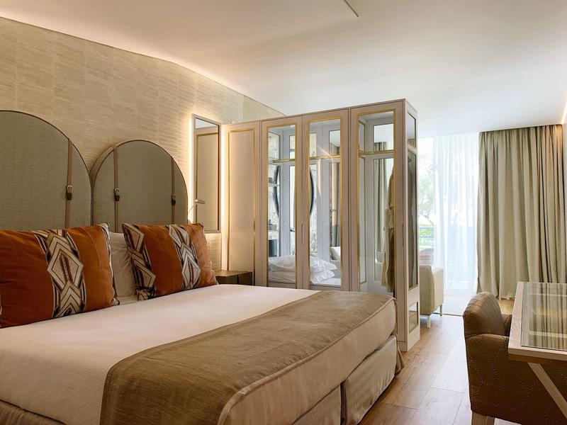 Camera d'hotel luminosa con letto matrimoniale, testiera elegante, cuscini e tende.