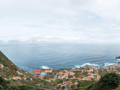 Blick auf ein Küstendorf mit roten Dächern und Meer im Hintergrund, umgeben von Hügeln.