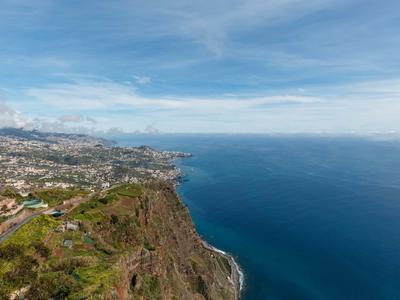 Blick auf steile Küste mit Stadt und blauem Meer unter bewölktem Himmel.