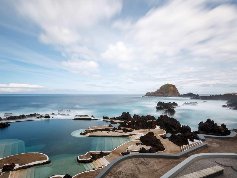 Natürlicher Meerwasserpool mit Felsen, blauem Himmel und leicht bewölktem Horizont.