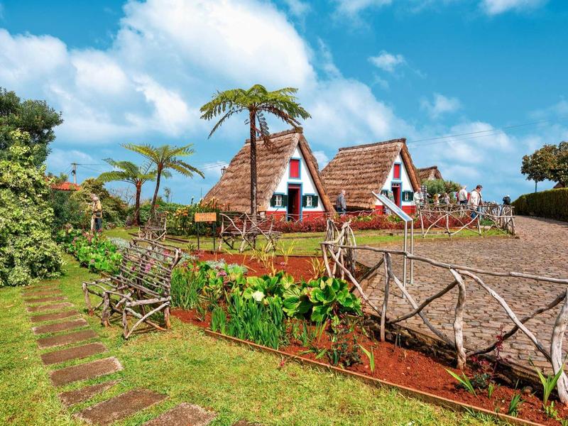 Typische strohgedeckte Häuser mit Dreiecksgiebeln, umgeben von grünem Gras und Holzzaun bei blauem Himmel.