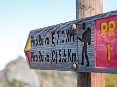 Wegweiser mit Entfernungen zu Pico Ruivo auf einem Wanderweg mit Bergblick.