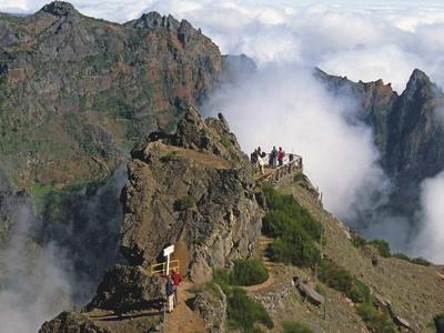 Bergpfad mit Wanderern und Wolken um umgebende Berge.