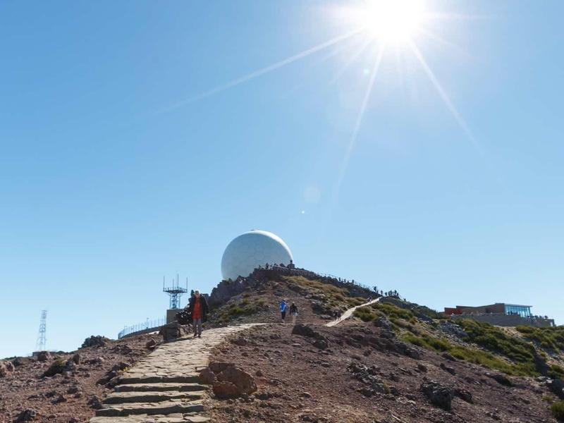 Steinweg führt zu weißer Kugelstruktur auf felsigem Hügel unter strahlendem blauen Himmel.