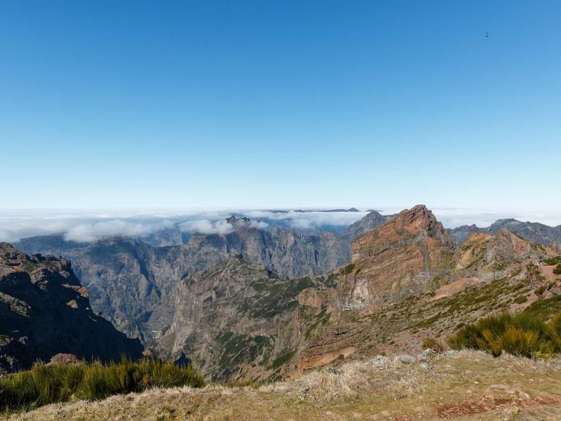 Berglandschaft mit felsigen Gipfeln, grünem Buschwerk und klarem blauem Himmel.