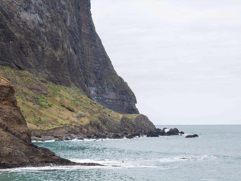 Felsige Küste mit steilen Klippen und ruhigem, blauem Meer darunter, bewölkter Himmel.