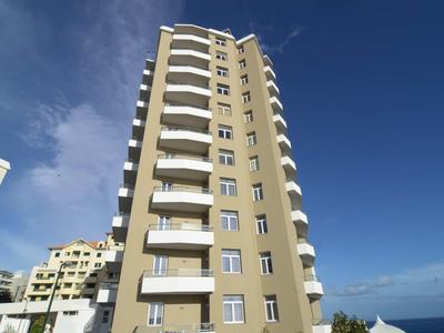 Wysoki budynek mieszkalny z wieloma balkonami pod niebieskim niebem.