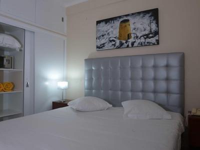 Nowoczesny pokój hotelowy z dużym łóżkiem, tapicerowanym zagłówkiem i podświetlanym stolikiem nocnym.