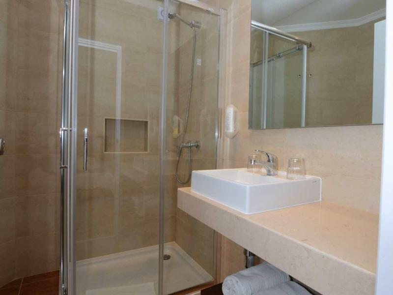 Kleines Badezimmer mit Glasdusche, rechteckigem Waschbecken auf beige Theke und weißen Handtüchern.