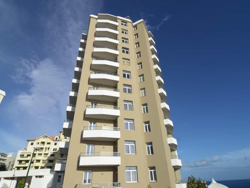 Hohes Wohngebäude mit weißen Balkonen und gelb-beigem Fassadenanstrich bei klarem Himmel.