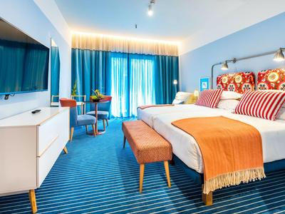 Modern hotelkamer met twee bedden, blauw tapijt en oranje accenten.