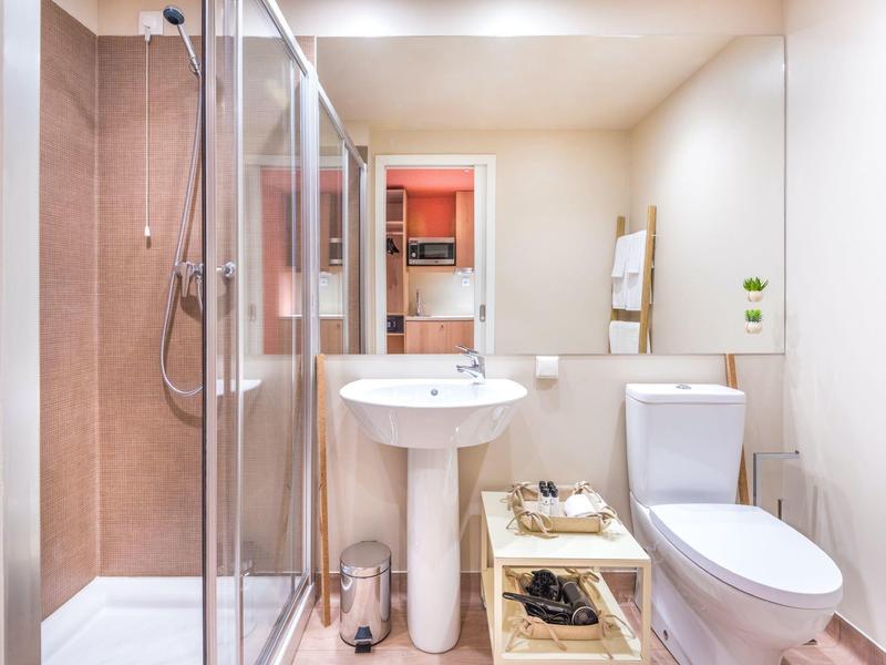 Helles Badezimmer mit Dusche, Waschbecken, Toilette, großem Spiegel und Holzregal.