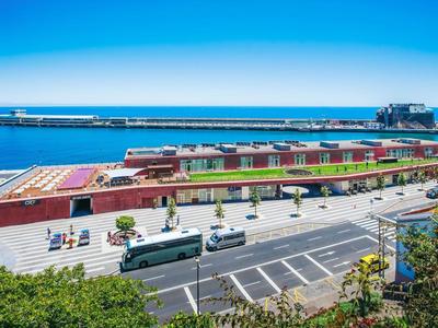 Uitzicht op een havengebied met parkeerplaatsen, bussen en een grote scheepssteiger bij heldere lucht.
