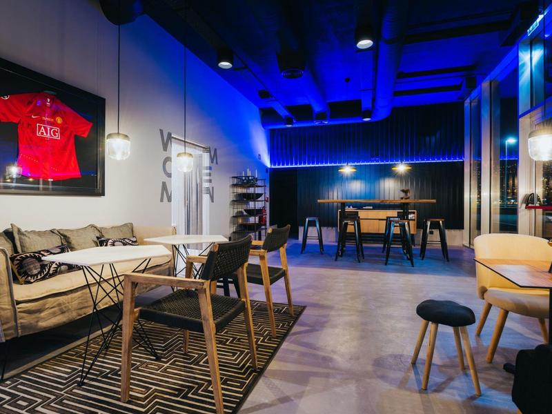 Moderne Lounge mit gemütlichen Sitzplätzen, Holzstühlen, Teppichen und blauem Neonlicht.