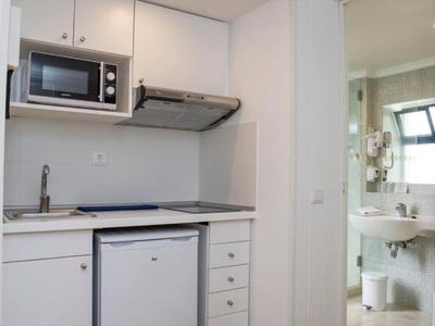 Small hotel kitchenette with microwave, fridge, sink, and stove in a white room.