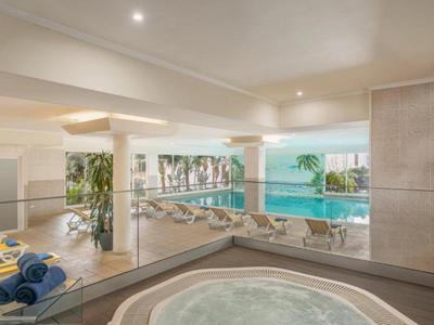 Moderner Innenpool mit Whirlpool, Liegestühlen, großen Fenstern und hellen, glatten Oberflächen.