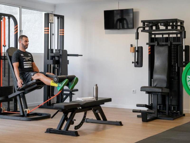 Mann trainiert mit Beinpressegerät in hellem, modernem Fitnessraum mit Fitnessgeräten und Holzfußboden.