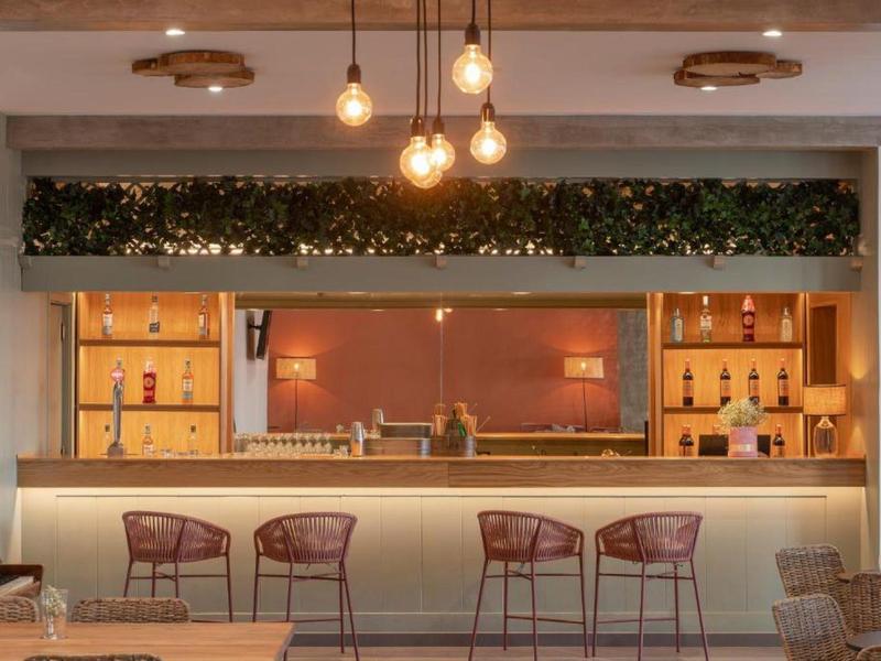 Moderne Bar mit Holztheke, vier roten Barhockern, hängenden Lampen und dekorativen Pflanzen.