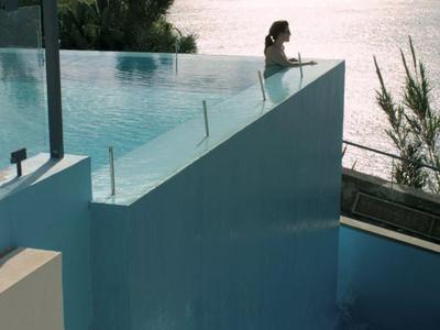 Mujer en piscina infinita con vistas al mar y montañas al atardecer.