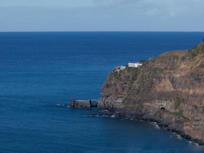 Scogliere con un edificio bianco sul bordo sopra il mare blu calmo sotto un cielo nuvoloso.