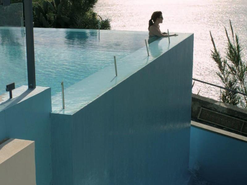 Una persona si gode una piscina a sfioro con vista sul mare e sulle montagne sullo sfondo.