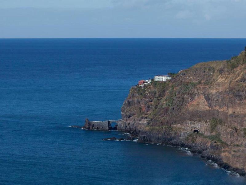 Scogliere con un edificio bianco sul bordo sopra il mare blu calmo sotto un cielo nuvoloso.