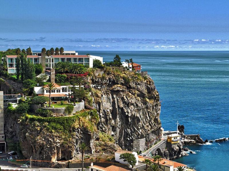 Hotel su una scogliera rocciosa con vista sul mare blu e cielo limpido.
