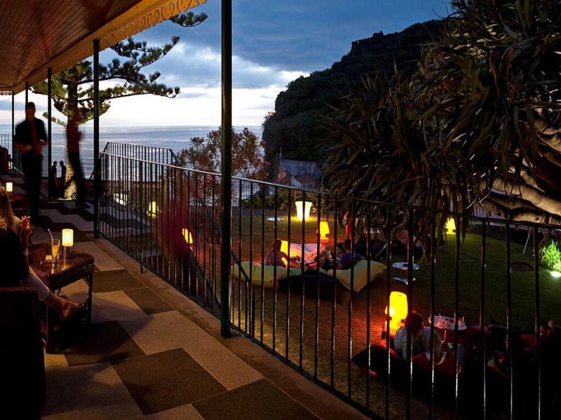 Terrazza serale con illuminazione, ospiti e vista su una collina boscosa.