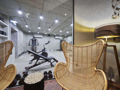 Binnenzicht op een moderne fitnessruimte met fitnessapparatuur en twee rotan stoelen op de voorgrond