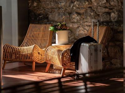 Twee gevlochten stoelen en een koffer voor een stenen muur in een zonovergoten kamer.