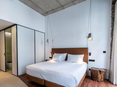 Modernes Schlafzimmer mit großem Bett, hölzernem Kopfteil, Holzstuhl, weißen Wänden und Beleuchtung hängt von der Decke.