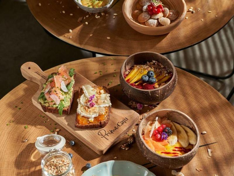 Teller mit Pfannkuchen, drei Schalen mit Desserts, Gläser mit Wasser und Kräutern auf Holztischen.