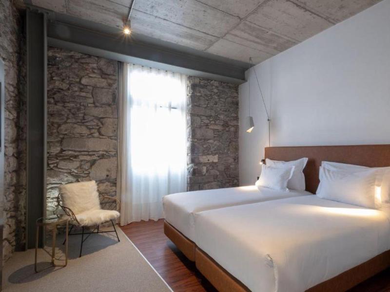 Modernes Schlafzimmer mit Steinmauer, großem Bett, Stuhl, Teppich und natürlichem Licht am Fenster.