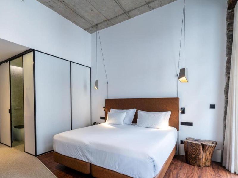 Modernes Schlafzimmer mit großem Bett, hölzernem Kopfteil, Holzstuhl, weißen Wänden und Beleuchtung hängt von der Decke.