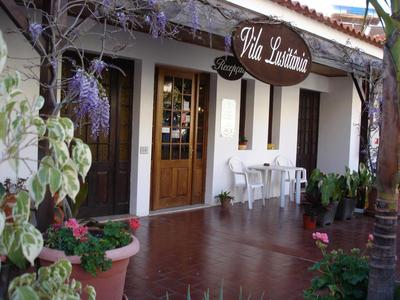 Area d'ingresso di un hotel con porte in legno e vetro e grandi piante in vaso.