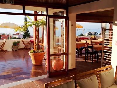 Vista dall'interno verso una terrazza con piante e ombrelloni al tramonto.