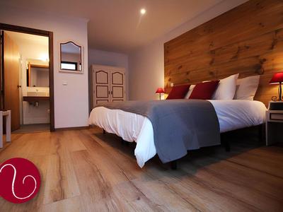 Camera d'hotel accogliente con letto matrimoniale, pavimento in legno e lampade moderne ai lati del letto.