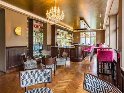 Elegante Hotelbar mit Holzboden, Kronleuchter und stilvollen Sitzbereichen mit gemusterten und pinken Stühlen.