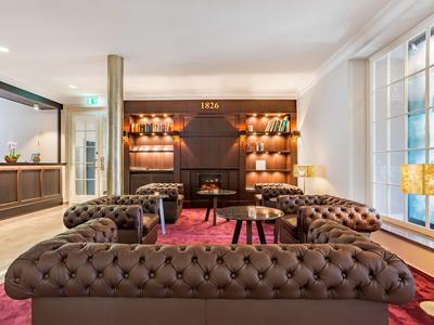 Modernes Wohnzimmer mit braunen Chesterfield-Sofas, rotem Teppich und großem Fenster mit Lampe.