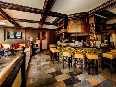Cozy hotel bar with wooden beams, stone floor, and yellow cushioned stools around a counter.