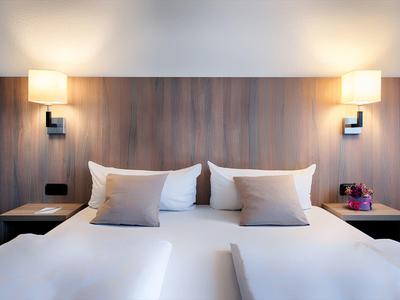 Modern hotel room with two single beds, wooden headboard, and bedside lamps