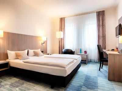 Modern eingerichtetes Hotelzimmer mit Doppelbett, Sitzbereich und Schreibtisch unter warmem Licht.