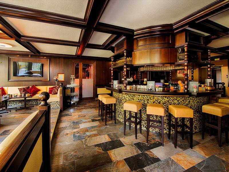 Cozy hotel bar with wooden beams, stone floor, and yellow cushioned stools around a counter.