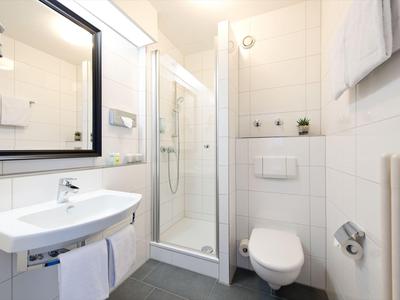 Kleines modernes Badezimmer mit Dusche, Waschbecken, Toilette und großem Spiegel.