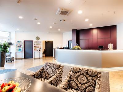 Helle Empfangshalle mit großem Tresen, zwei gemusterten Sesseln und modernen Dekorationen.