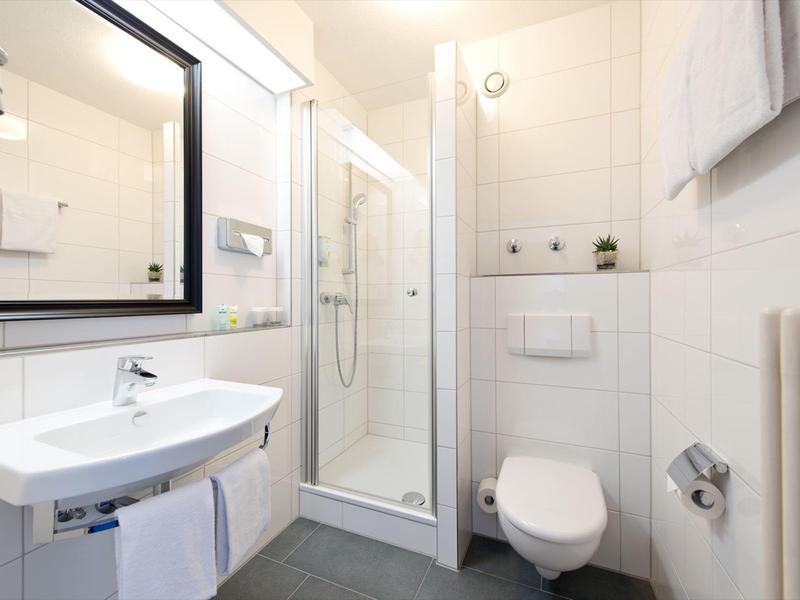 Moderno baño de hotel luminoso con ducha, lavabo e inodoro en blanco.