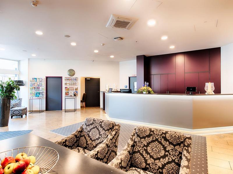 Área de recepción de hotel luminosa con mostrador y asientos cómodos en tonos cálidos.