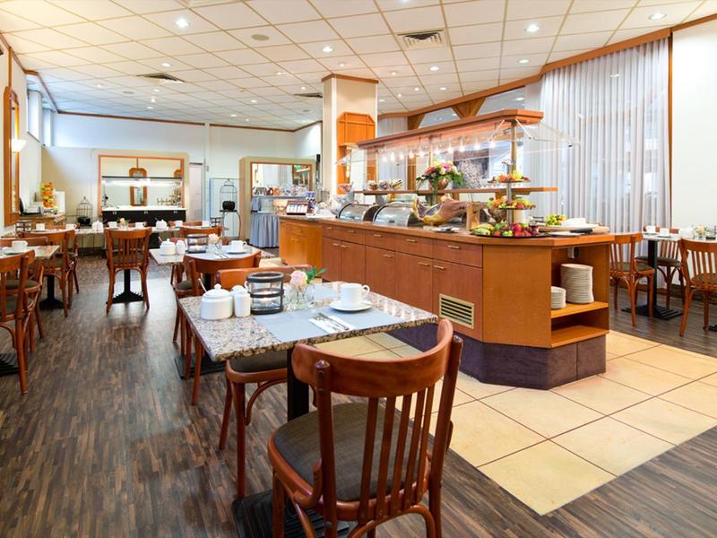 Restaurante de hotel luminoso con sillas de madera, mesas puestas y área de buffet a la luz del día.